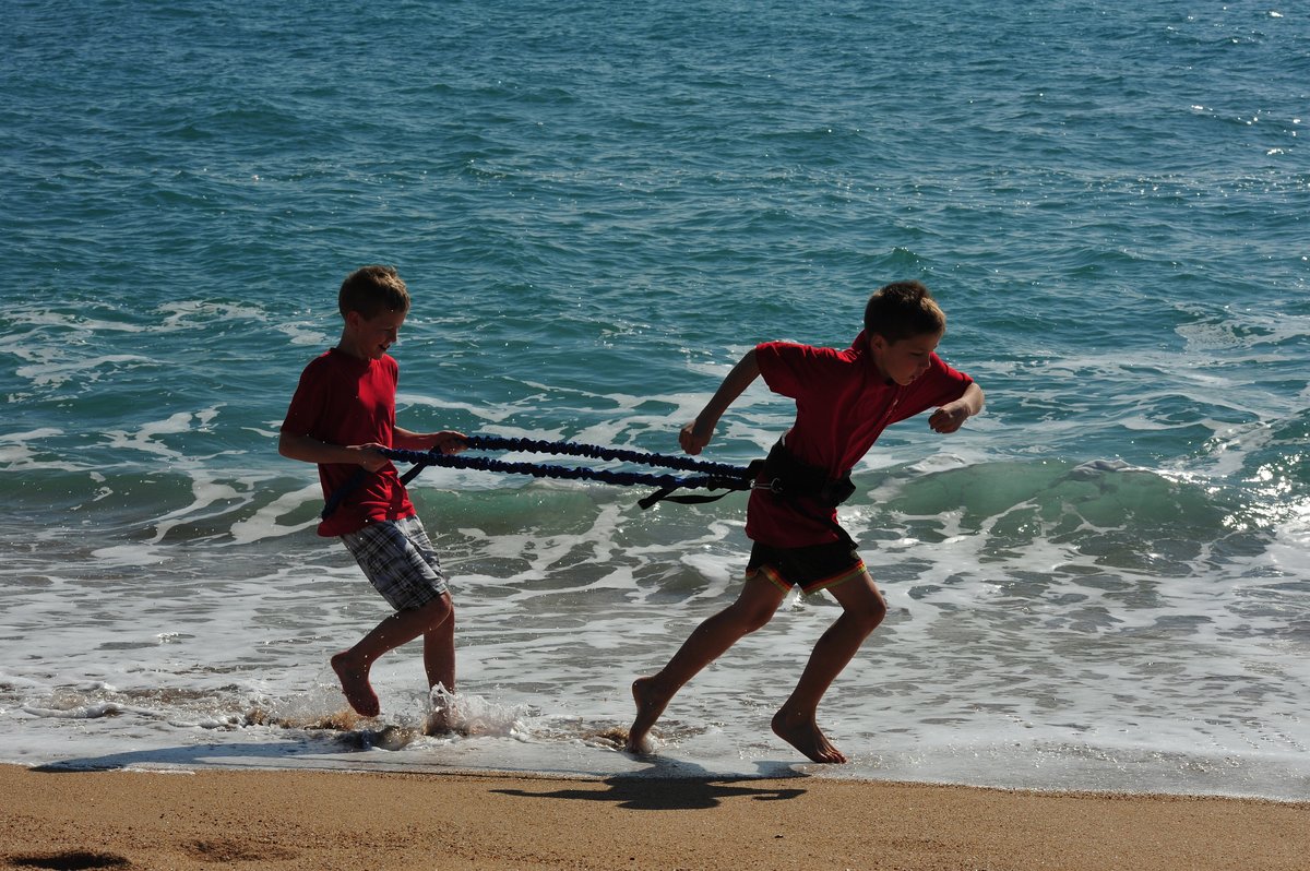 Zwei junge Sportler trainieren am Strand einen Antritt mit einem Widerstandsband.